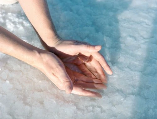 Close-up of a fair-skinned adult holding water in their hands over a textured, light blue and white mineral surface in an outdoor setting.