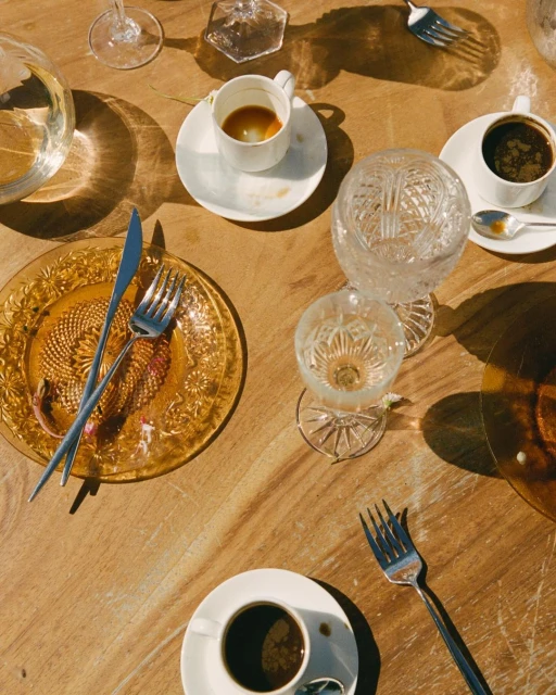 Overhead shot of an amber glass plate with flatware, crystal glasses, and coffee cups on a wood table with warm, natural lighting.