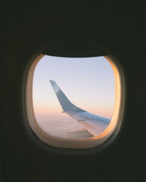 Airplane wing seen through the window of an airplane during flight with a light blue and pink sky at sunset or sunrise.