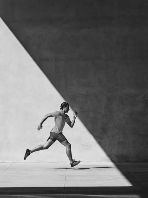 Monochrome image of a man running in a light-filled urban space, athletic apparel, dynamic composition, black and white photography.