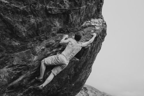 Monochrome shot of a shirtless adult male rock climbing on a textured rock formation in an outdoor environment.