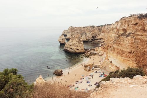 Scenic view of Praia da Marinha in Algarve, Portugal, featuring sandstone cliffs, a sandy beach with people, and the Atlantic Ocean.