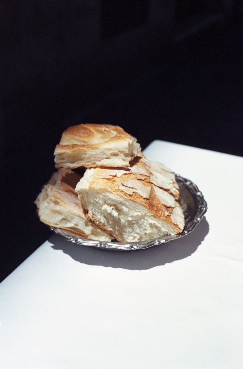 Close-up of sliced bread piled on a small silver tray, set against a stark contrast of a white table and a dark background.