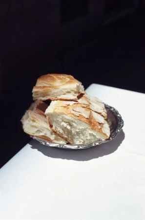 Close-up of sliced bread piled on a small silver tray, set against a stark contrast of a white table and a dark background.