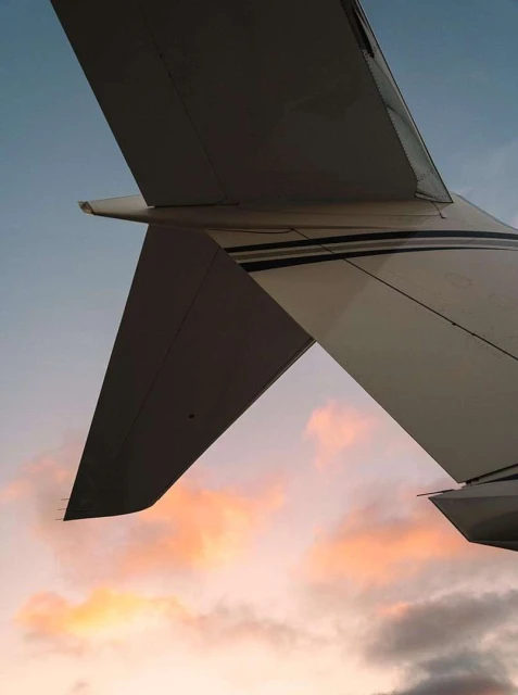 Airplane wing and tail fin with a sunset backdrop featuring hues of orange, pink, and purple blending into the blue sky at dusk.