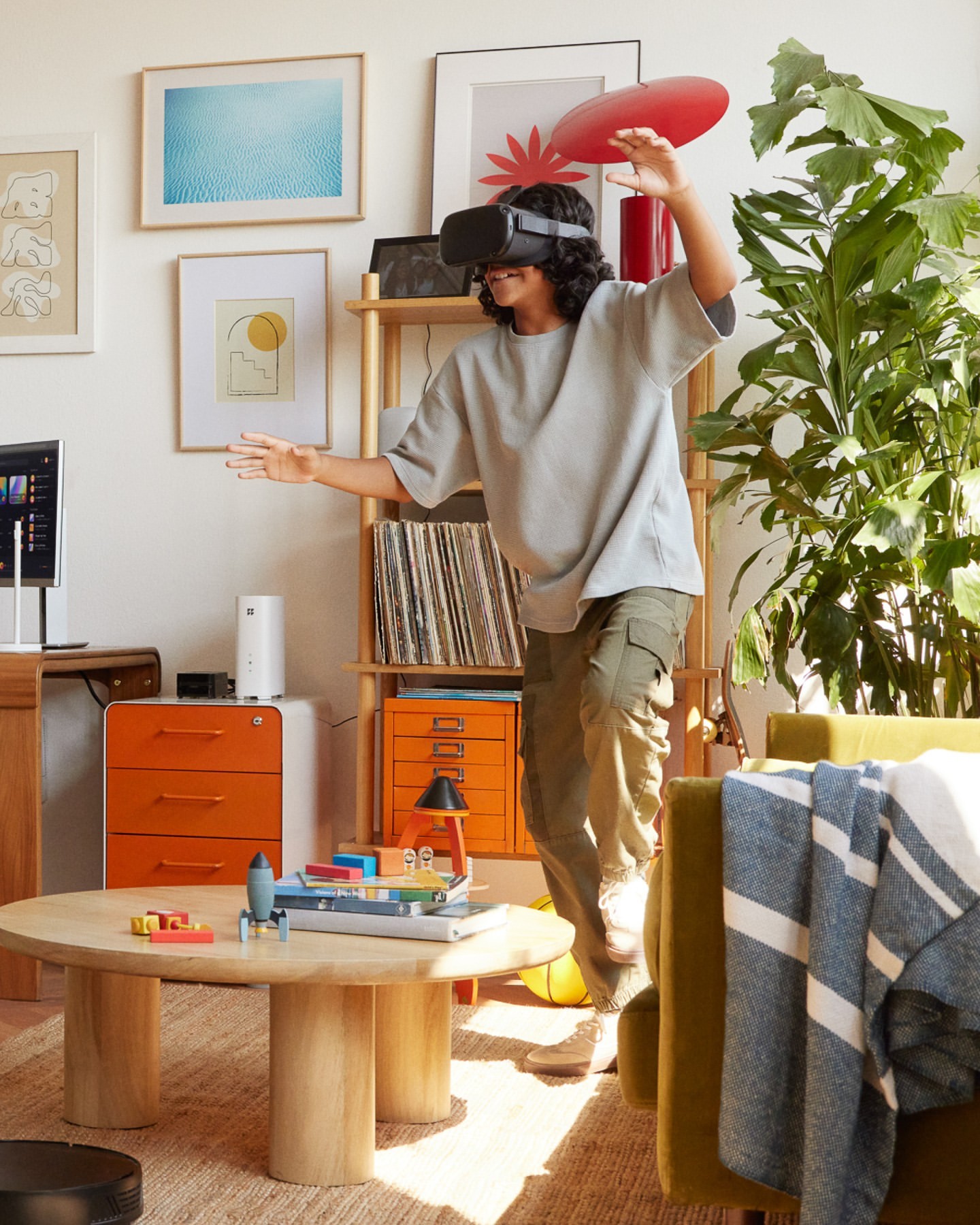 Woman with VR headset and red disc in modern living room; indoor setting with natural light, beige walls, and wooden furniture.