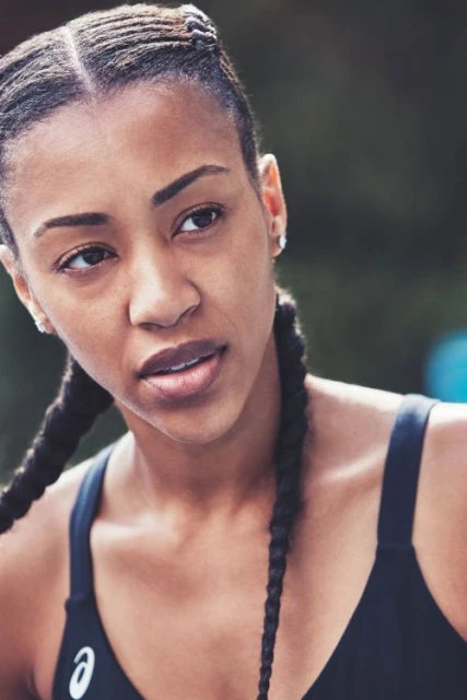 Portrait of a Black woman with braided hair wearing a sports bra, looking off-camera against a blurred outdoor background.