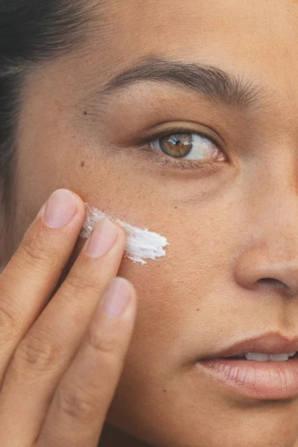 Close-up shot of a woman applying white cream to her face with her fingers, focusing on skincare and beauty routine.