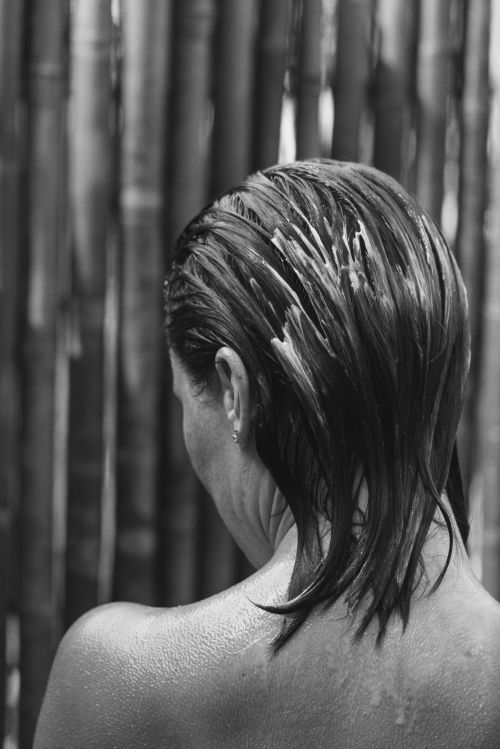 Back view of a woman with wet hair, showcasing the texture and light reflecting on the strands against a bamboo background.