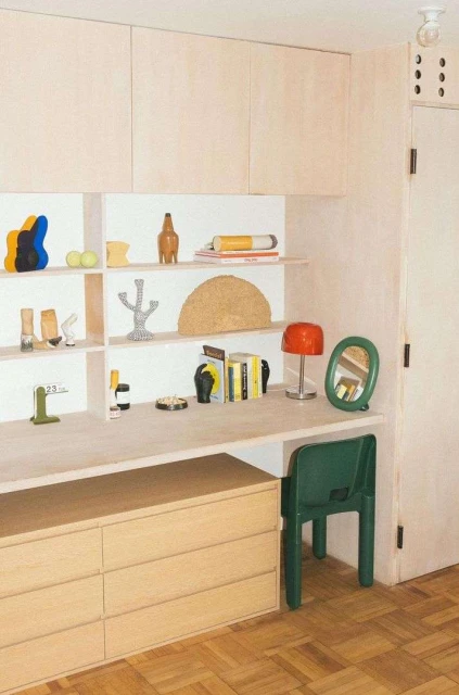 Interior view of a modern study area featuring light wood cabinetry, a desk, a chair, and various decorative objects on shelves and desk.