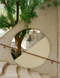 Architectural shot of concrete stairs with a circular opening framing a tree trunk and a hanging metal bell
