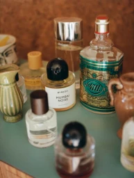 Collection of various perfume bottles and small ceramic vases arranged on a green tabletop