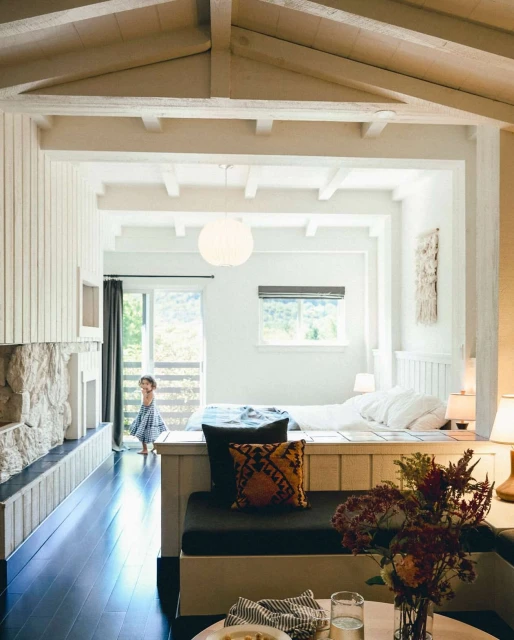 Bright interior showcases a child by open patio doors, leading to a view of trees and hills, plus living and sleeping spaces.