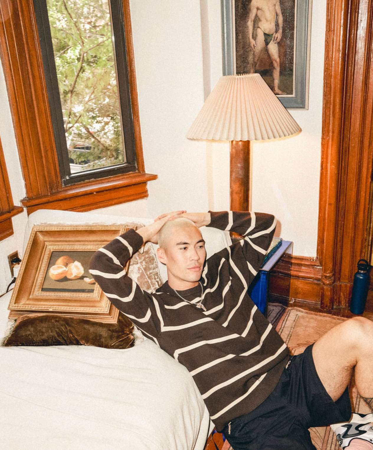 Man with shaved blonde hair seated on a white couch wearing a brown striped sweater, photographed by Anna Wolf