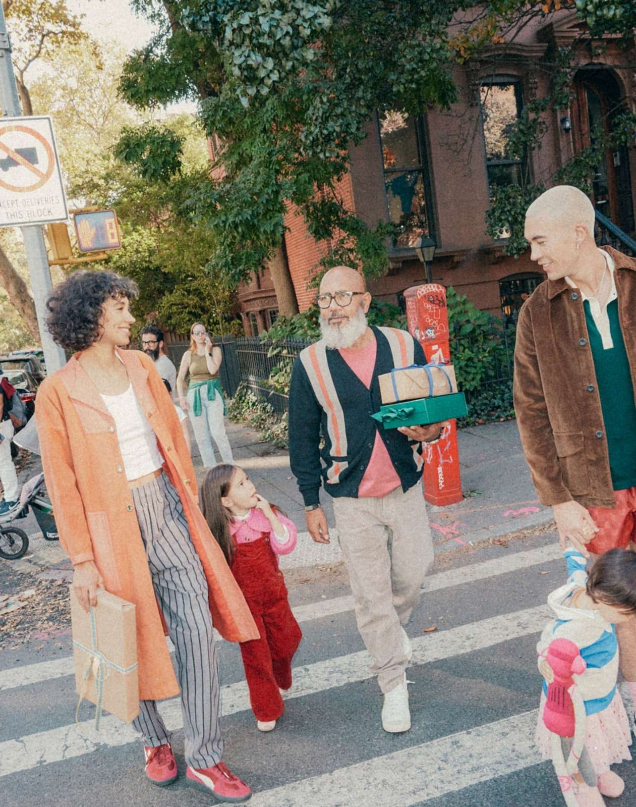 A group of people walks across a crosswalk in an urban environment on a sunny day carrying gifts, including adults and children.