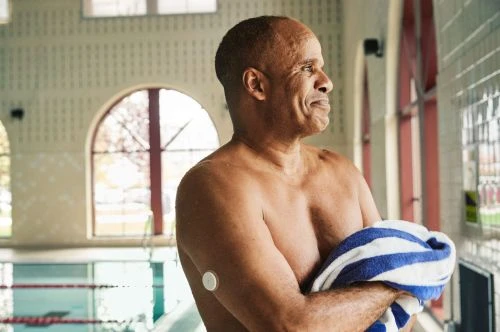 An older man holding a blue and white striped towel near an indoor swimming pool, photographed by Anna Wolf.