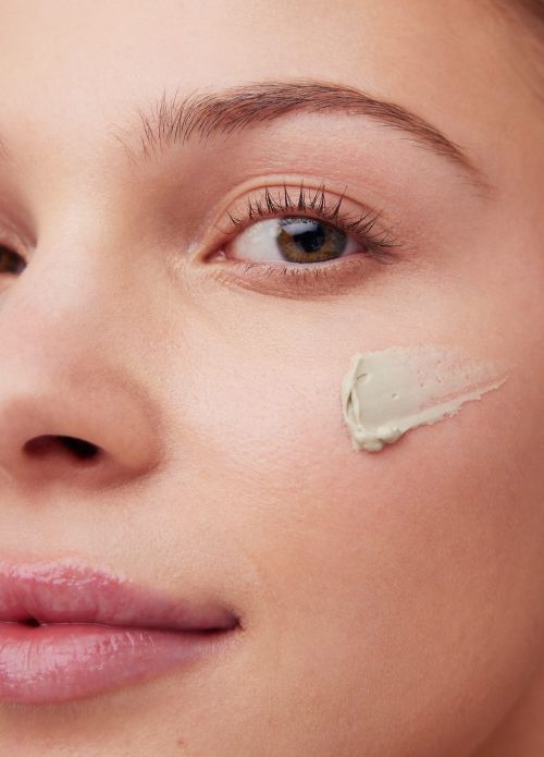 Close-up of a woman's face with cosmetic clay applied on her cheek, emphasizing skincare and facial care in a beauty context.