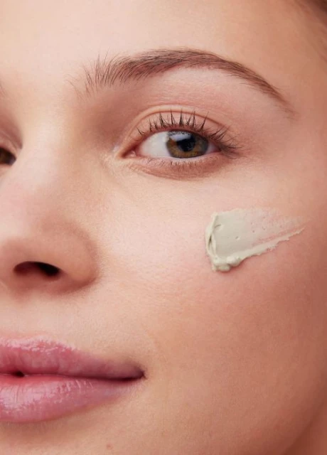 Close-up of a woman's face with cosmetic clay applied on her cheek, emphasizing skincare and facial care in a beauty context.