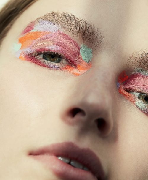Close-up portrait of a woman wearing painterly pastel eyeshadow in pink, orange, and mint green by Anna Wolf