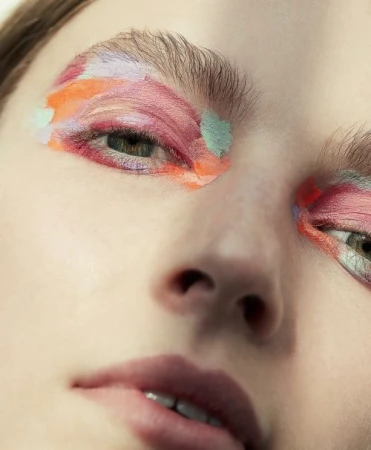 Close-up portrait of a woman wearing painterly pastel eyeshadow in pink, orange, and mint green by Anna Wolf