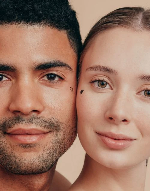 Close-up portrait of a couple against a neutral background. The man has short dark hair and a beard. The woman has light hair.
