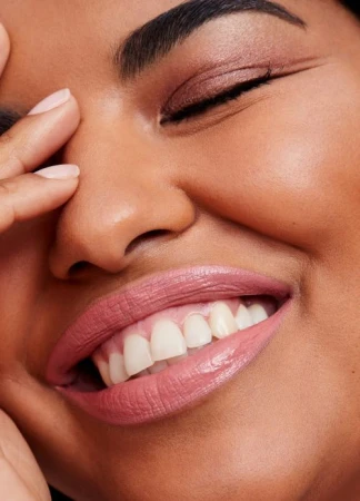 Close-up portrait of a smiling woman showing glossy pink lipstick and soft eye makeup, photographed by Anna Wolf.