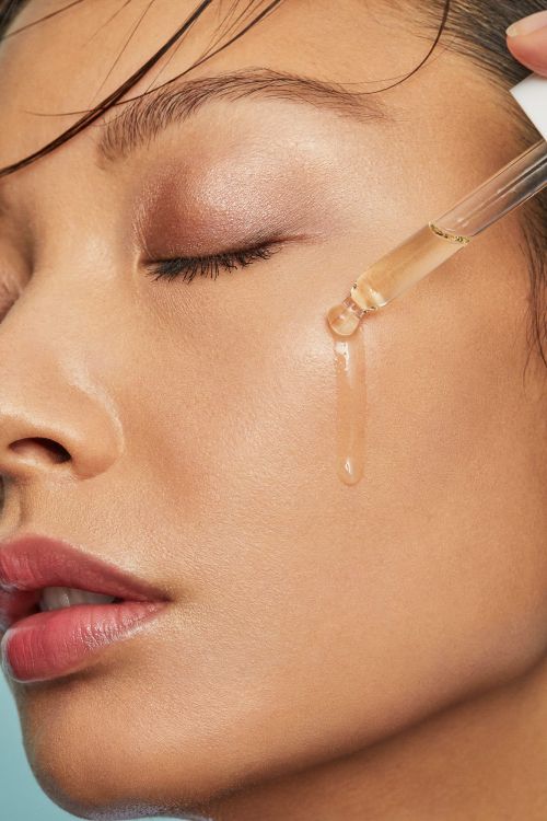 Close-up of a woman applying serum to her face with a dropper, showcasing skincare and beauty treatment in a minimalistic setting.