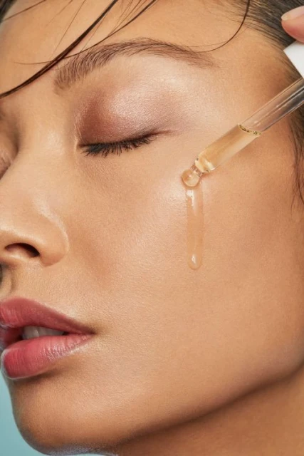 Close-up of a woman applying serum to her face with a dropper, showcasing skincare and beauty treatment in a minimalistic setting.