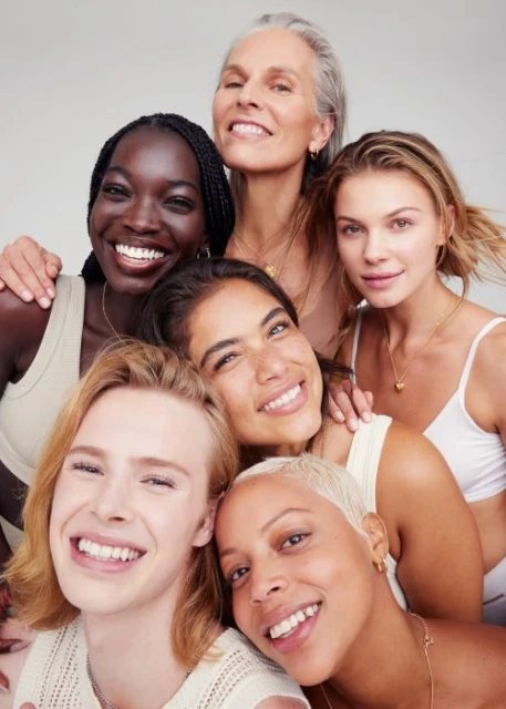 Diverse group portrait of six adult women with neutral skin tones smiling in a close, clustered composition on a bright background.