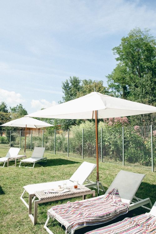 Outdoor leisure scene features lounge chairs with striped towels under white umbrellas on a green lawn, ideal for relaxation.