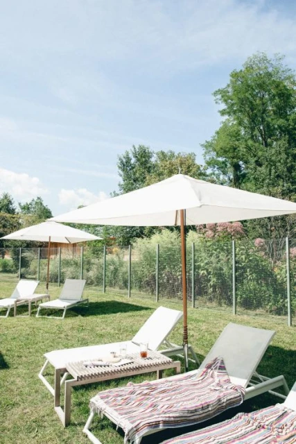 Outdoor leisure scene features lounge chairs with striped towels under white umbrellas on a green lawn, ideal for relaxation.