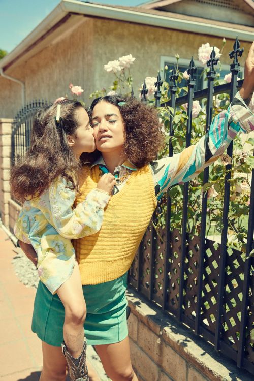 A woman holding a young girl who is kissing her cheek near a black iron fence outside a residential building.
