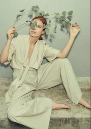 Red-haired woman seated wearing light green two-piece outfit holding eucalyptus branches