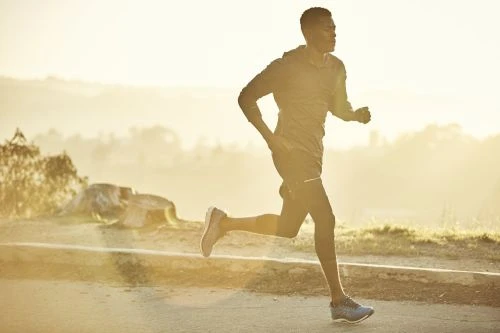Black man running outdoors on a paved path during sunset, captured in profile by Jeff Vallee
