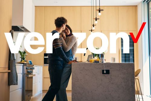 A couple embraces in a modern kitchen in front of a counter with breakfast, with the word Verizon overlaid on the image.