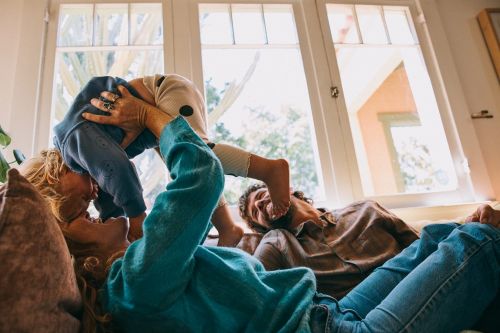 Mother and father playing with their child indoors near a window, creating a heartwarming family moment.