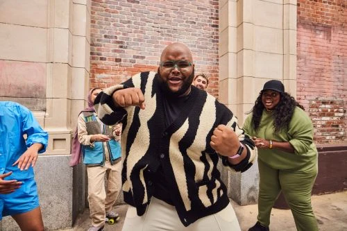 Dynamic group of diverse adults dancing in front of a brick wall, vibrant energy and urban setting. Fashionable knitwear and casual attire.