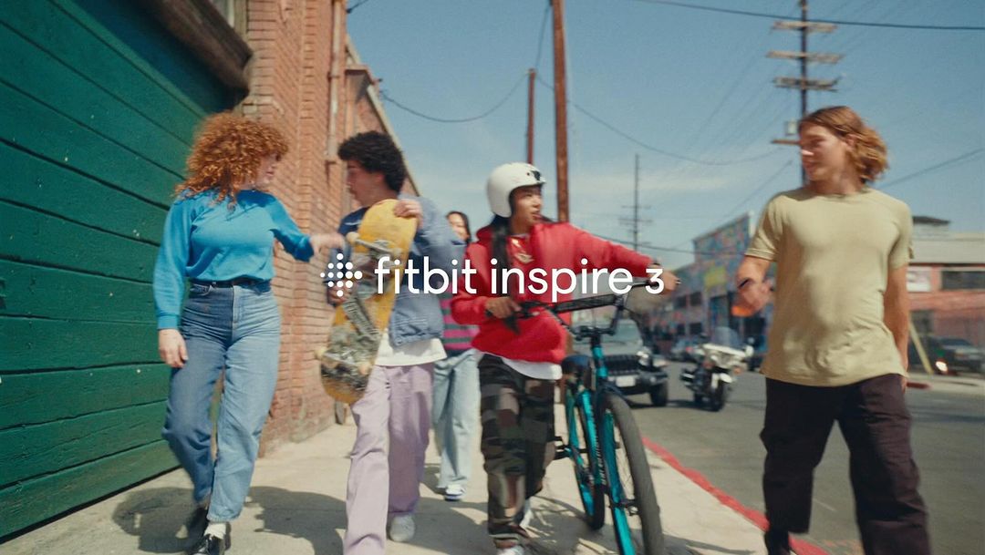 Group of young friends walking down an urban sidewalk together, carrying a skateboard and a bicycle.
