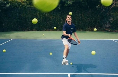 Tennis player on a blue court surrounded by floating yellow tennis balls, captured by Jeff Vallee.