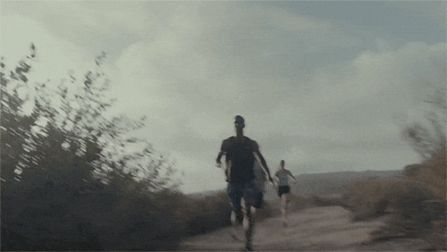 Two athletes run a rugged outdoor trail under a cloudy sky. One runner leads with the second athlete trailing behind. Scenic, outdoor fitness.