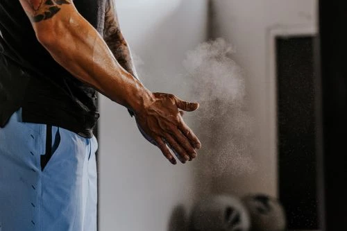Muscular man with tattoos claps hands with chalk dust in the air in a gym. Gym environment with white wall and fitness equipment.