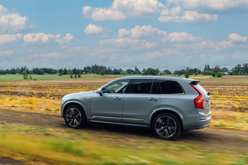 Silver SUV driving on a dirt road through a rural landscape with fields under a partly cloudy blue sky during the daytime.
