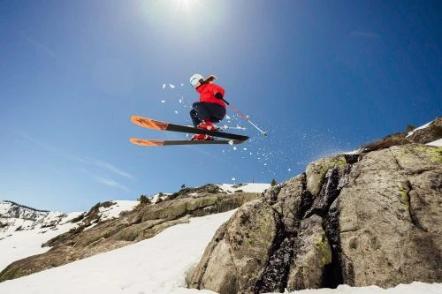 A skier in mid-air performs a jump against a bright blue sky, showcasing winter sports and mountainous terrain.