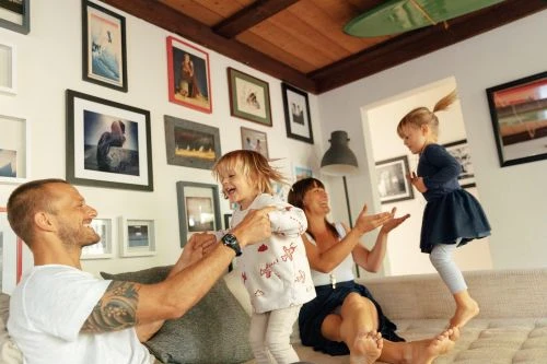 A happy family of four interacts playfully in their living room, with two young girls, a woman, and a man enjoying a lighthearted moment together.