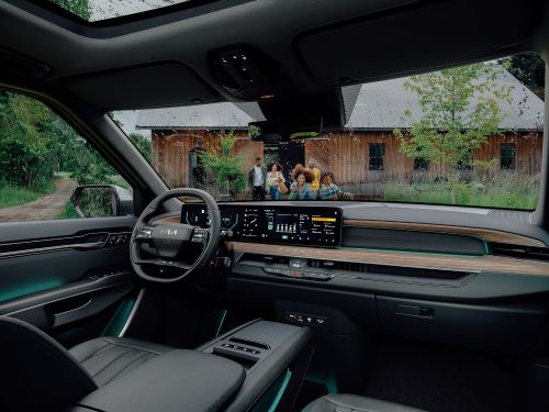 Car interior showcases sleek dashboard display, steering wheel, and family in the background, blending automotive design with lifestyle.