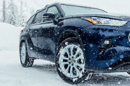 Navy blue SUV in the snow. Exterior shot of a four-door SUV with silver rims and snow covering the car and snowy environment.