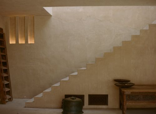 Minimalist interior featuring a beige color palette, showcasing an architectural staircase design, complemented by decorative bowls and an open shelf.