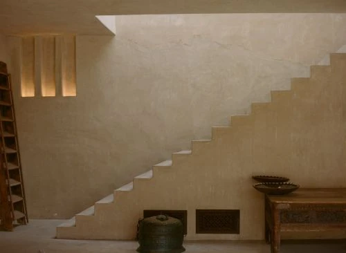Minimalist interior featuring a beige color palette, showcasing an architectural staircase design, complemented by decorative bowls and an open shelf.