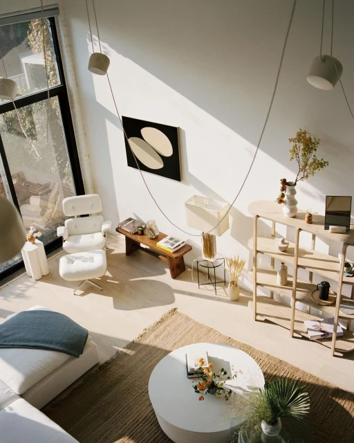 Living room interior with white modern furniture, area rug, abstract art, open-plan design, and natural light from a large window.