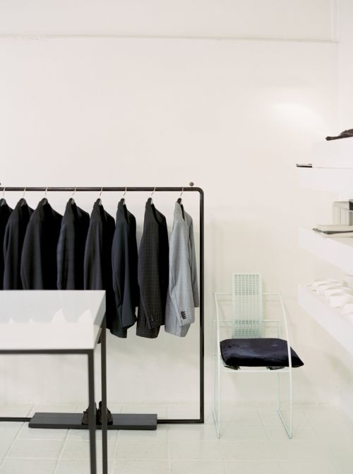 Minimalist clothing store interior with rack of dark jackets, white walls, and light-colored tile floor creating a bright, spacious retail environment.